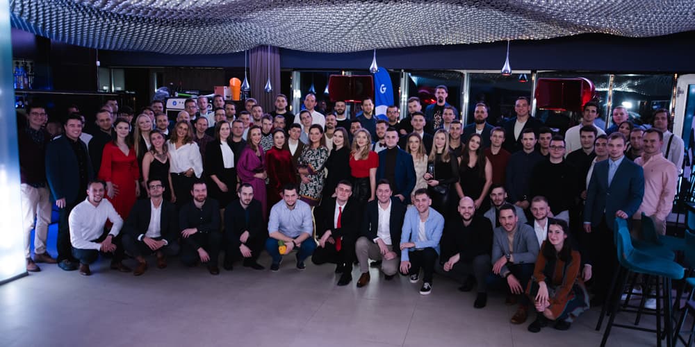 Skupinová fotografia celého tímu Goodrequest v interiéri počas spoločného podujatia, s členmi v formálnom a neformálnom oblečení, obklopenými dekoráciami a vybavením priestoru.