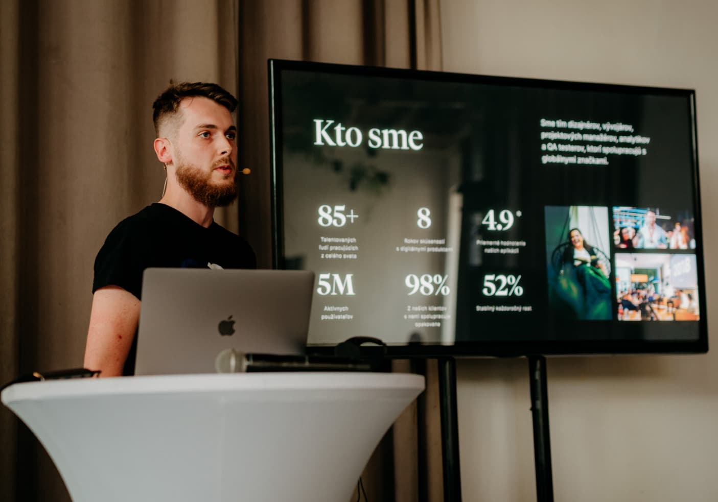 Prezentácia o spoločnosti Goodrequest s názvom „Kto sme“ zobrazená na veľkej obrazovke, vedľa ktorej stojí osoba pri stole s notebookom. Na obrazovke sú uvedené štatistiky o tíme, používateľoch, spokojnosti a raste.