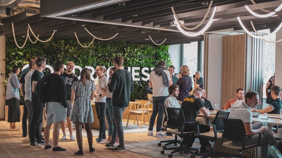 Novootvorený kancelársky priestor Goodrequest s moderným dizajnom, zelenou stenou s nápisom „GOODREQUEST“, štýlovým nábytkom a skupinami ľudí, ktorí diskutujú alebo pracujú počas slávnostného otvorenia.